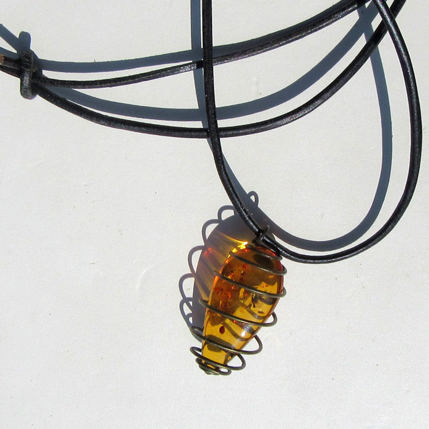 Flaches Bernsteinstück mit Einschlüssen am Lederband